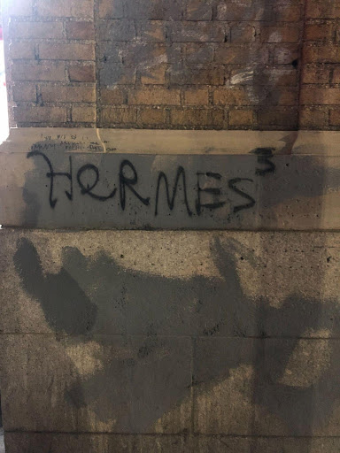 Picture taken at night of graffiti on a brick and concrete wall that reads 'Hermes3' in black spraypaint.